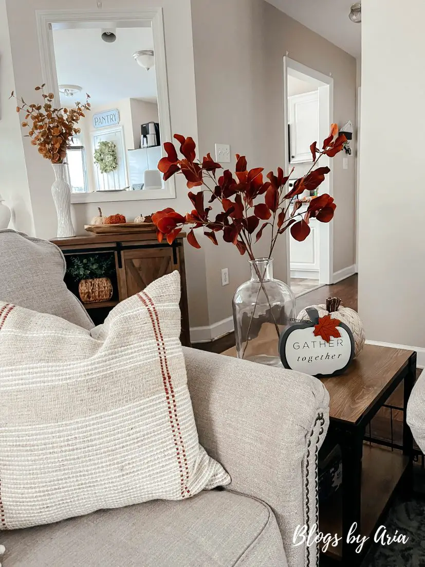 early fall decorating ideas with fall foliage in clear glass vase paired with textured neutral pillows