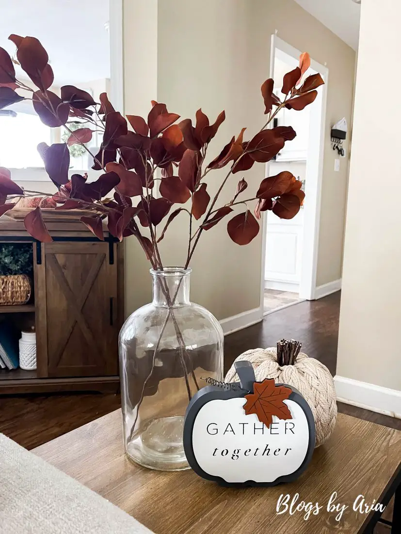 dark brown stems in glass vase with sweater knit pumpkin and pumpkin sign to create fall vignette