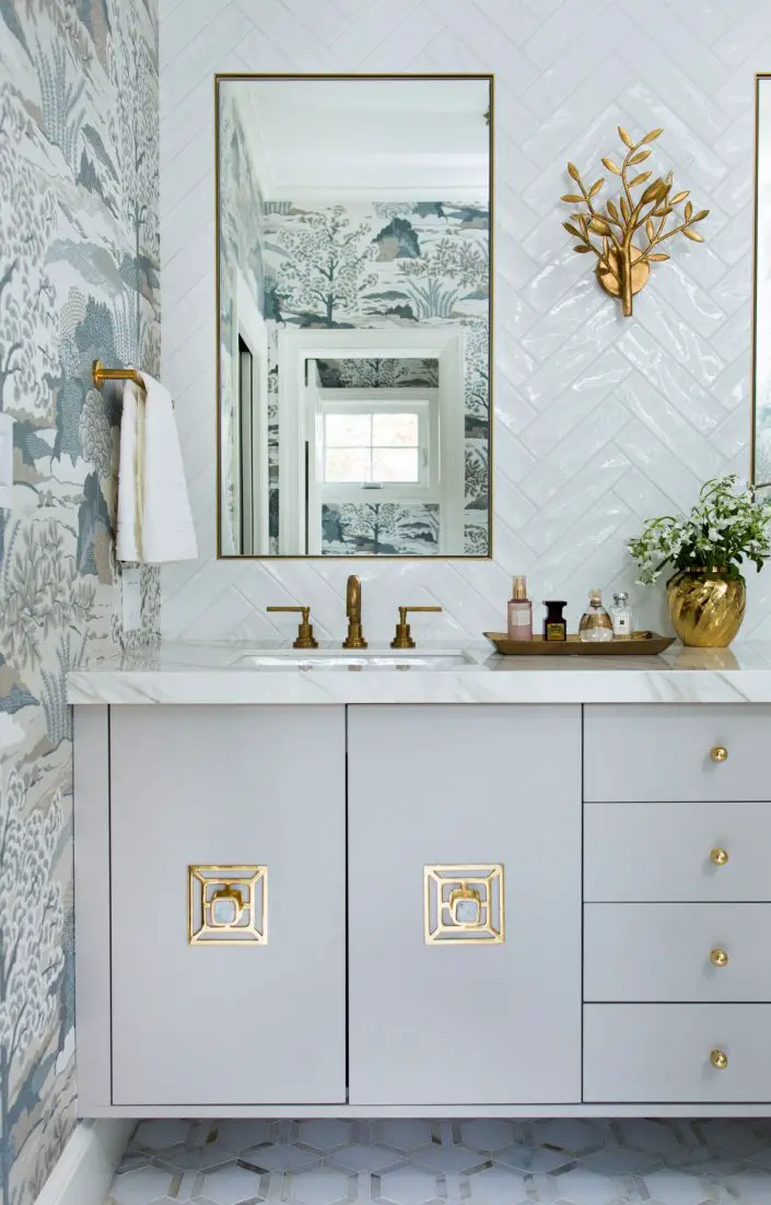 bathroom with herringbone tile backsplash, gold accents and serene wallpaper