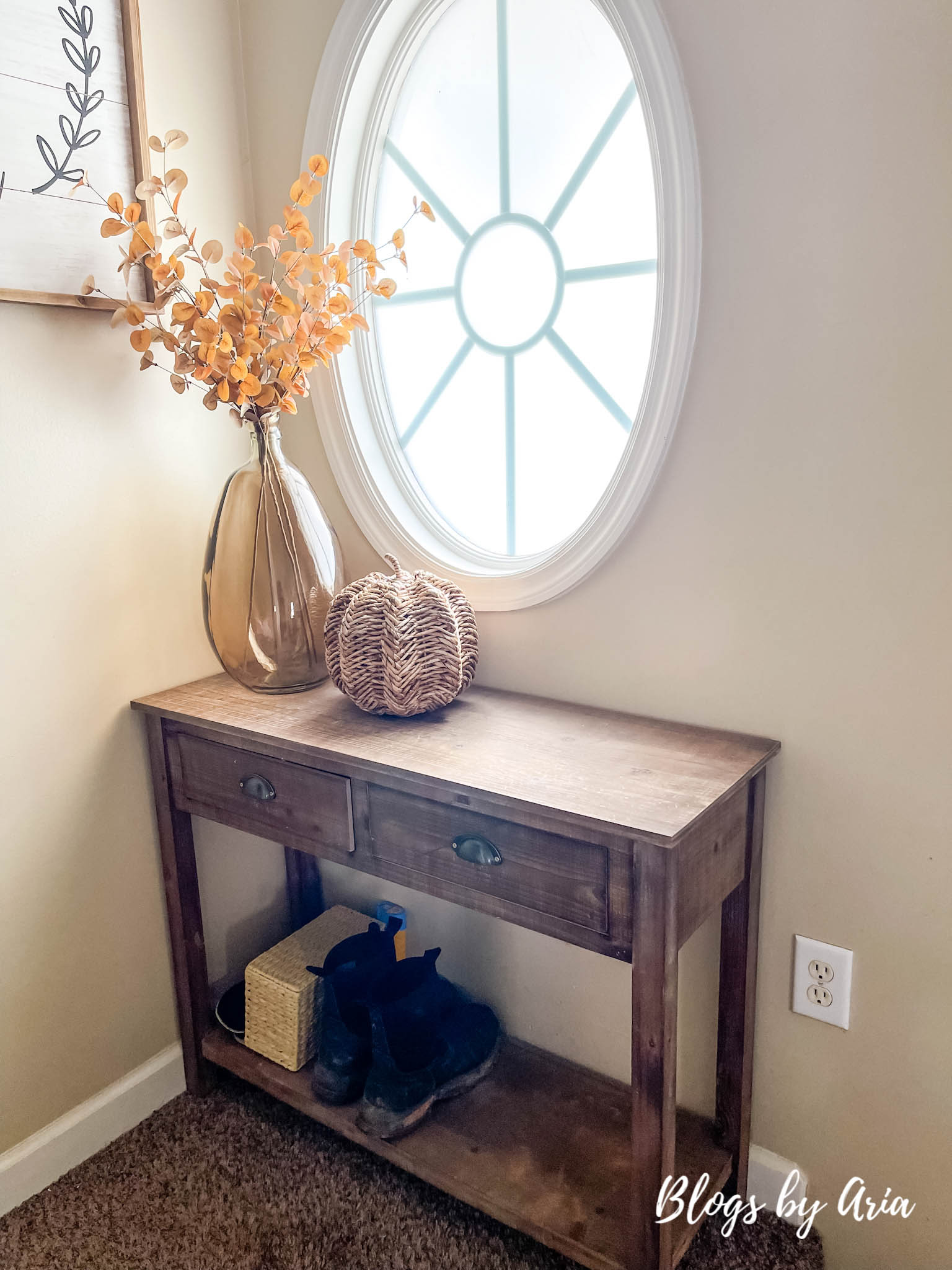 rustic entryway table styled for fall with large amber glass vase, golden brown eucalyptus stems and woven pumpkin