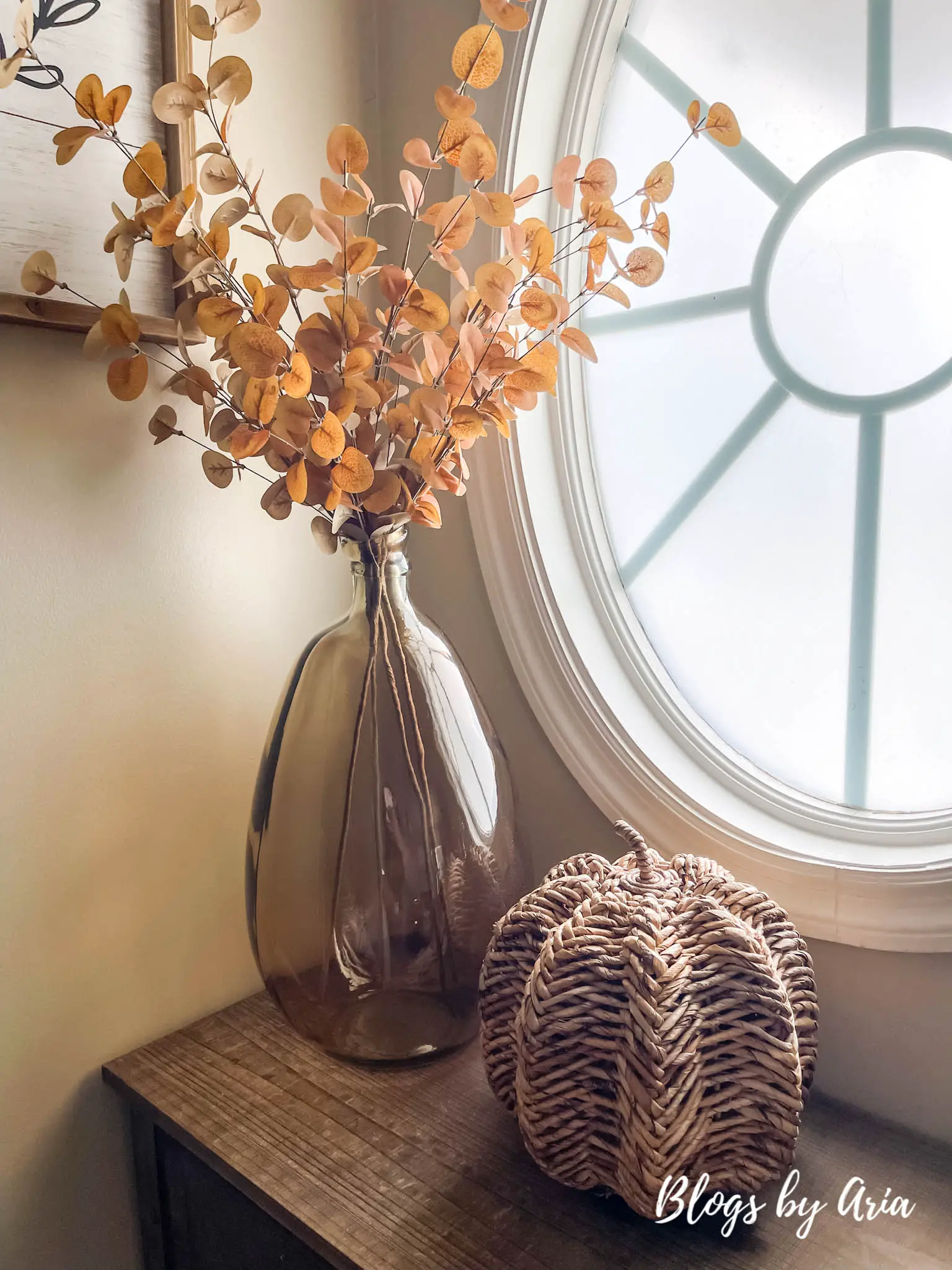rustic entryway table styled for fall with large amber glass vase, golden brown eucalyptus stems and woven pumpkin